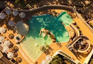 Parc aquatique vu du ciel : bassins, rochers et toboggans entourés de parasols