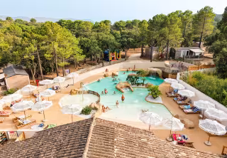 Parc aquatique entouré de parasols, de transats et de pins, avec les montagnes au fond