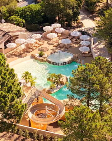 Vue aérienne du parc aquatique entouré de pins, avec ses parasols et son toboggan