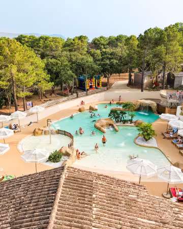 Parc aquatique entouré de parasols, de transats et de pins, avec les montagnes au fond